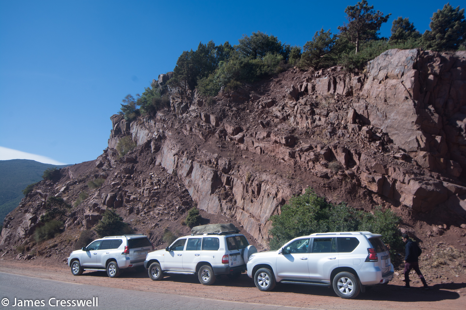 Vehicles at side of road in front of rock outcrop