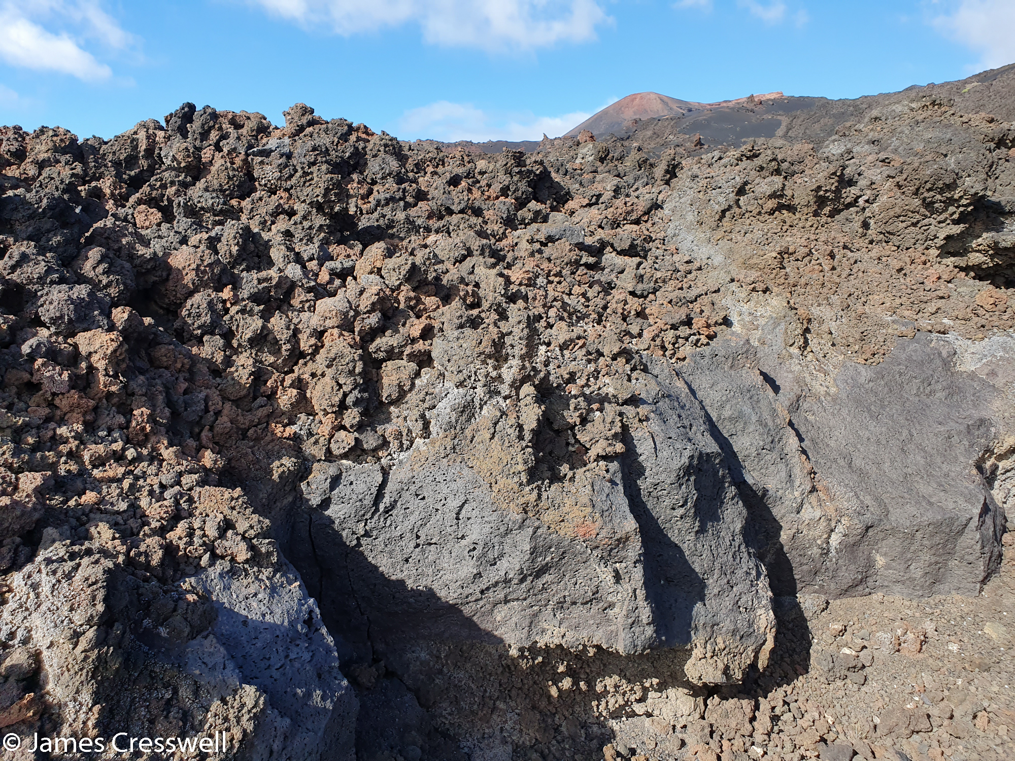 Solidified lava flow in the foreground with volcanic cone in the background