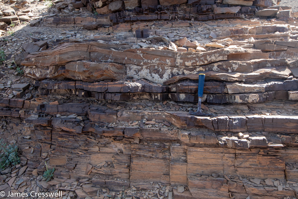 A photograph of a geological hammer resting on layers of rock