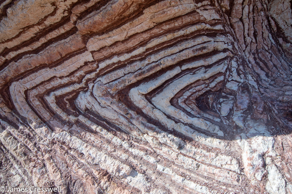A photograph of a red and white striped rock in a sideways 'V' shaped fold