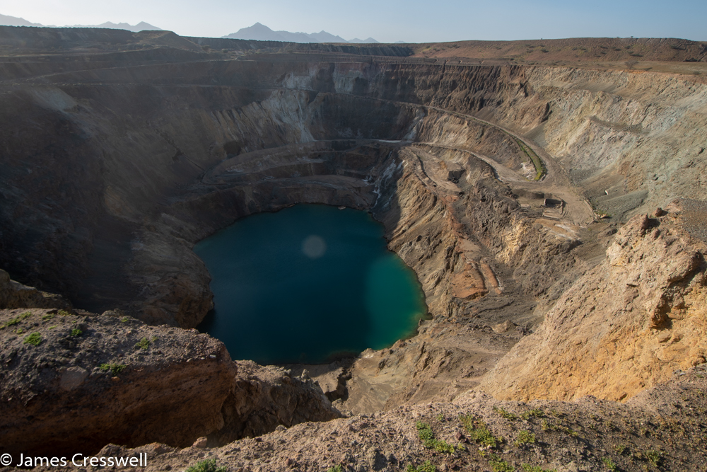 A photograph of a huge hole in the ground with a lake at its base