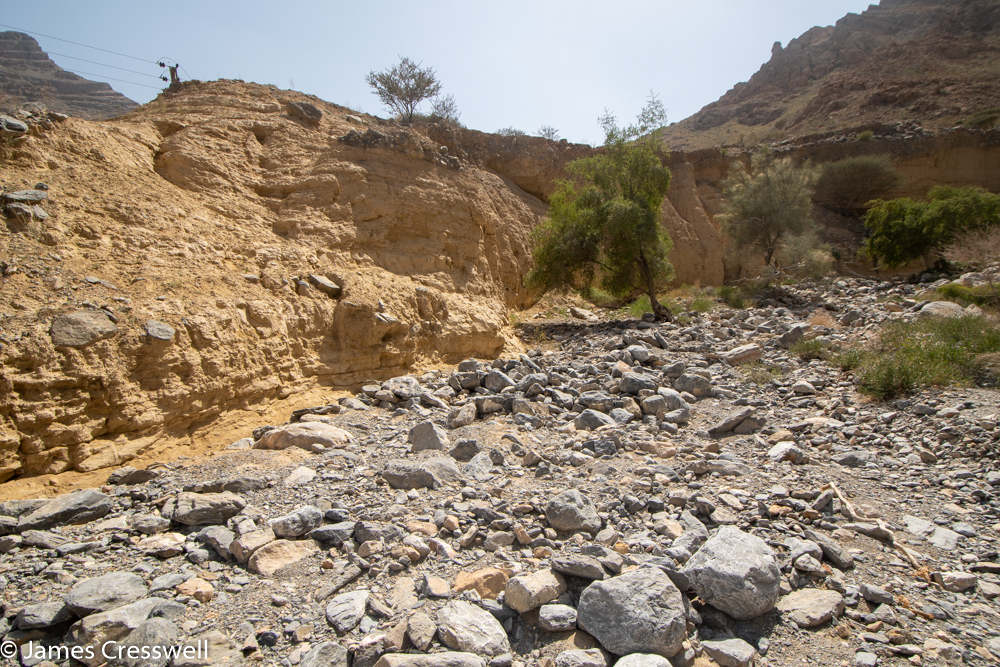 A photograph of a a yellow crumbly cliff, with grey boulders in the foreground