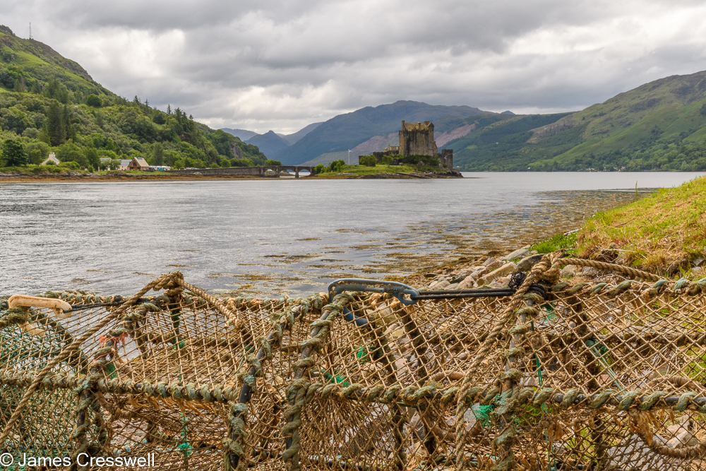 Lobster pots in the foreground with sea, a castle and mountains in the background