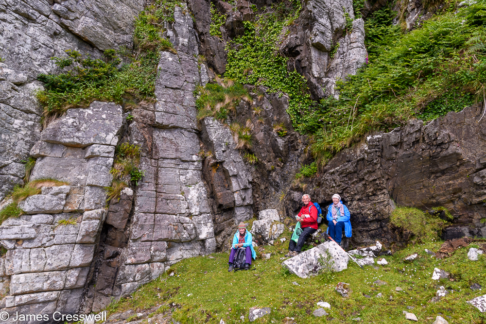Three people sit in front of a cliff