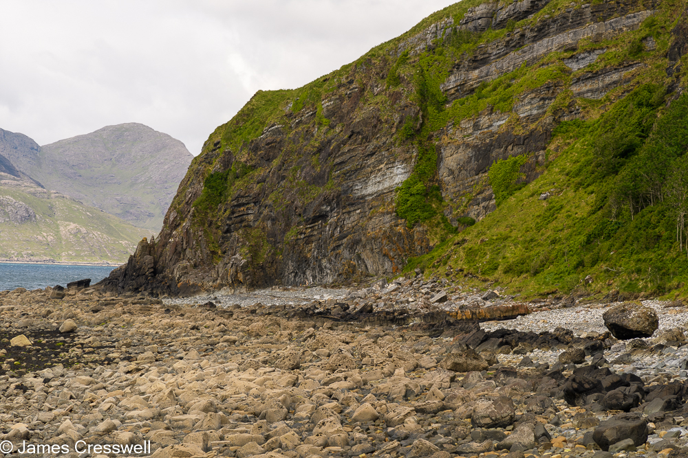 A boulder beach with a cliff behind
