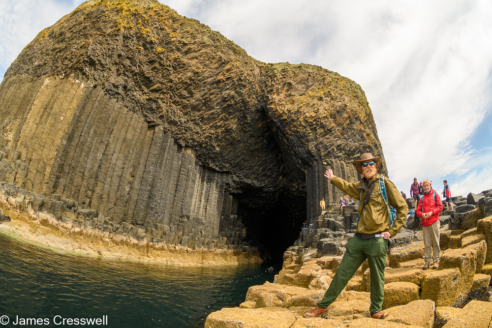 A man, James Cresswell, points to the entrance of a cave, Fingal's Cave