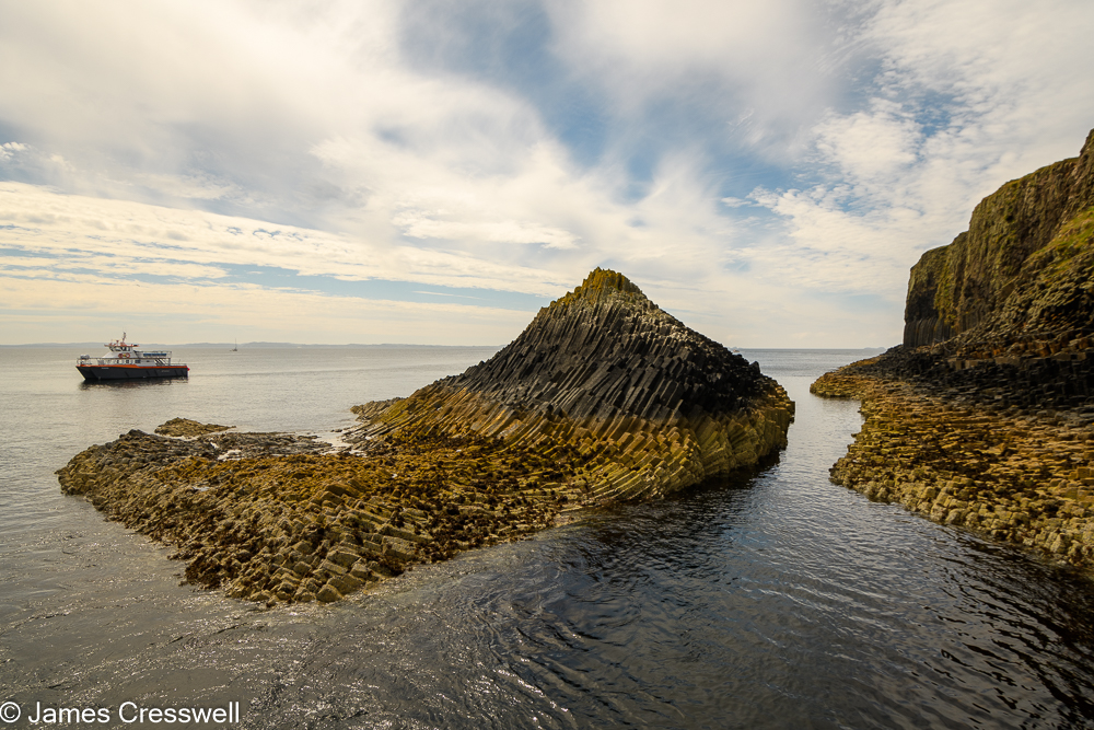 A shoreline with columnar basalt rocks and a boat