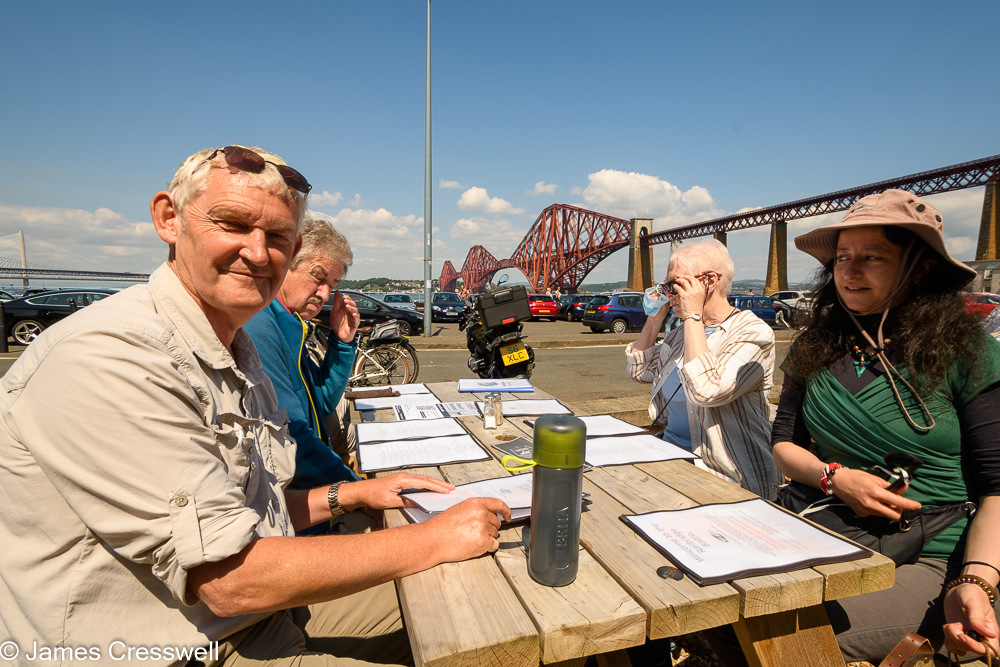 Four people sitting at a picnic table with a large red bridge in the background