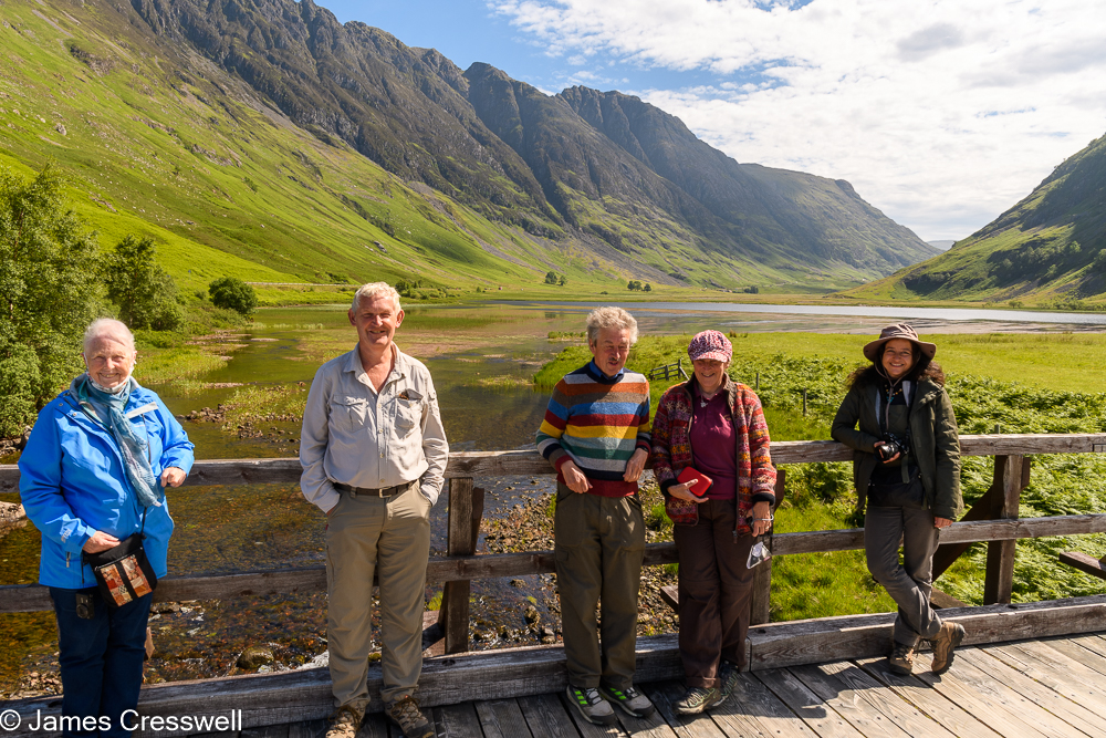Five people stand on a bridge with a U shaped valley in the background