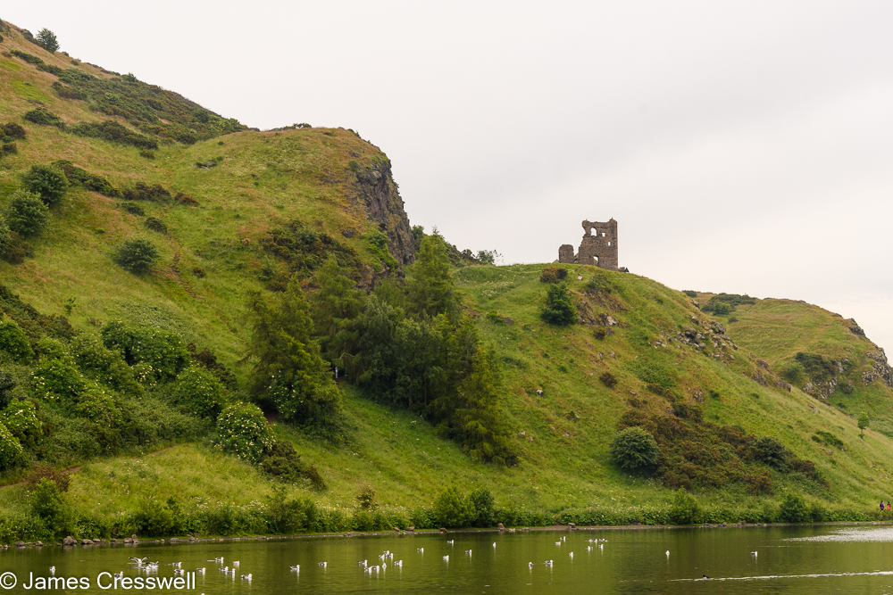A ruined castle on a rocky hill, with a lake in the foreground