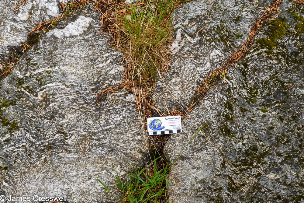 A scale card placed on top of rocks which contains wavy white bands