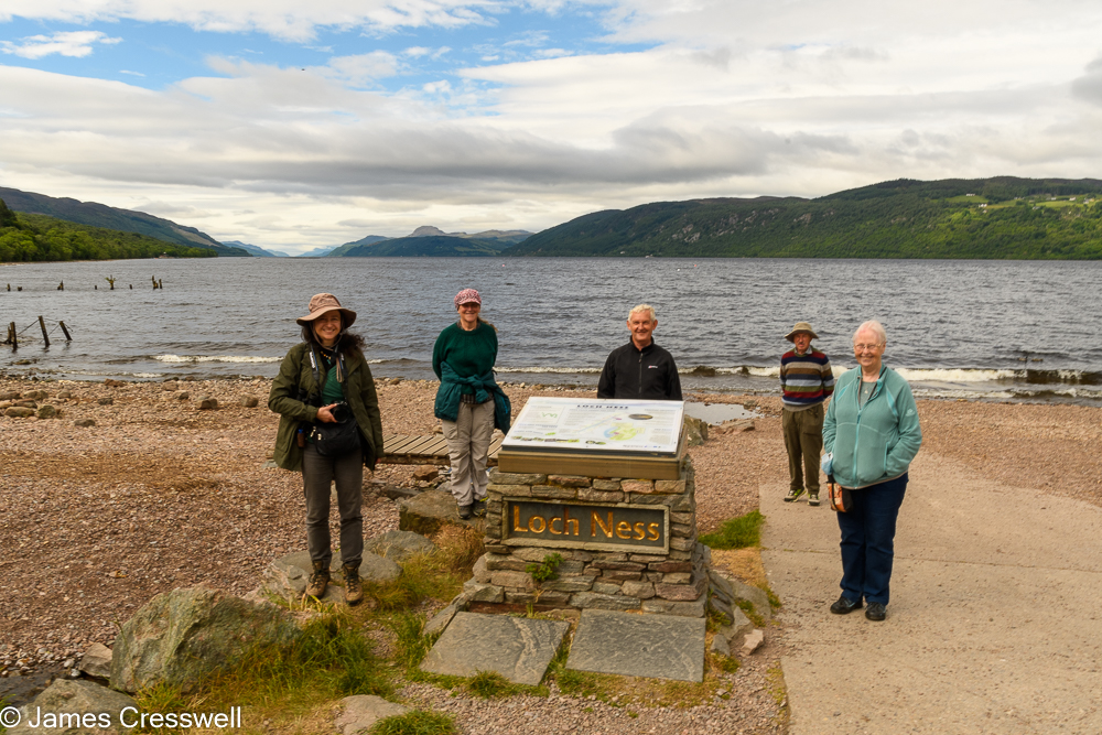 Five people stand next to a sign in front of a large lake
