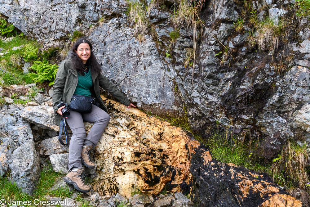 A woman points to the contact between yellow rocks on the bottom and grey rocks above