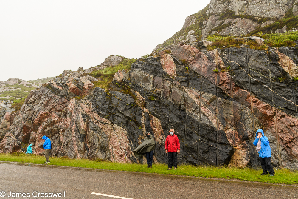 Five people stand in front of a colourful rocks in a road cutting