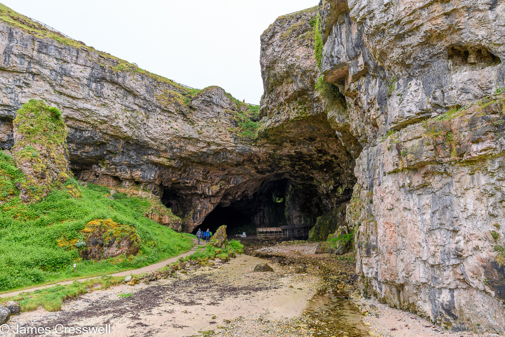 Two people walk into a large cave entrance