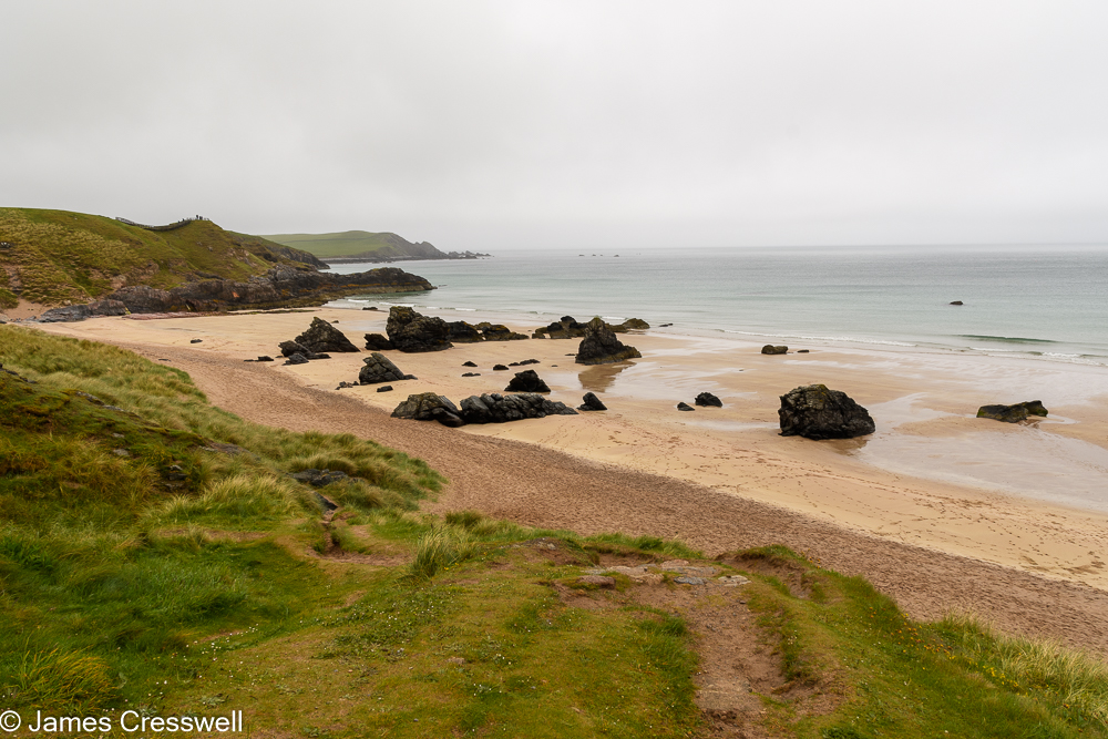 View over a sandy beach that contains rocky outcrops