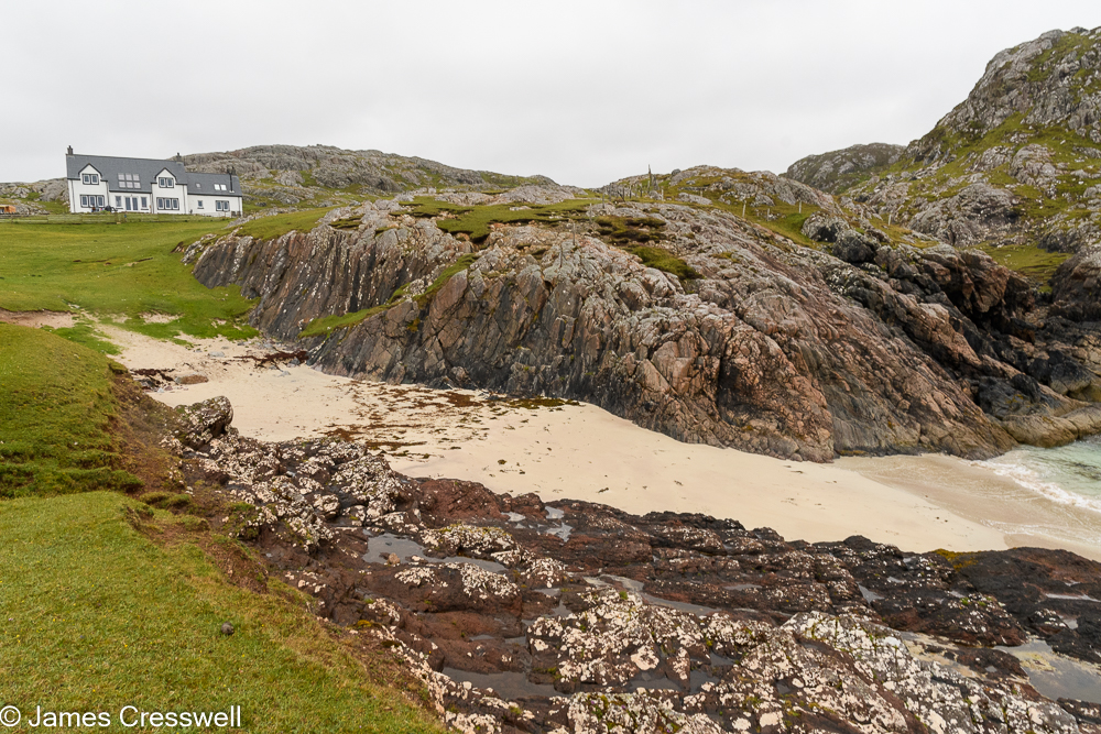 A photograph of a rocky shoreline, containing the world's largest boulder, with a house in the background