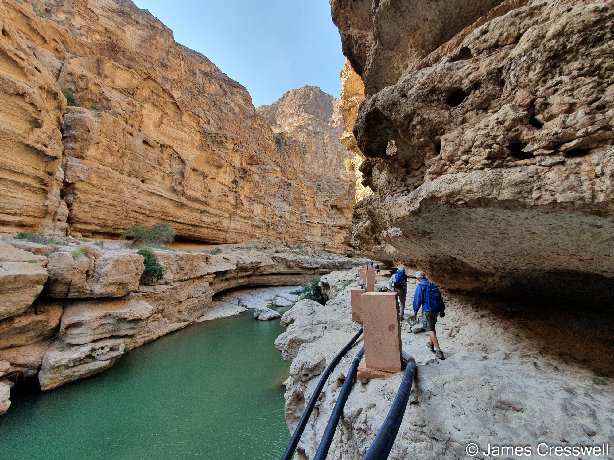 People walking alongside water in a rock-cut canyon