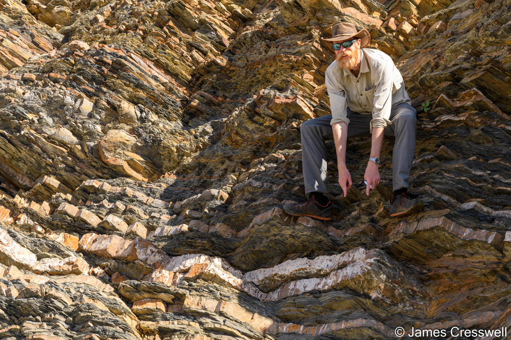 Man pointing to the hinge of a fold in turbidite sediments