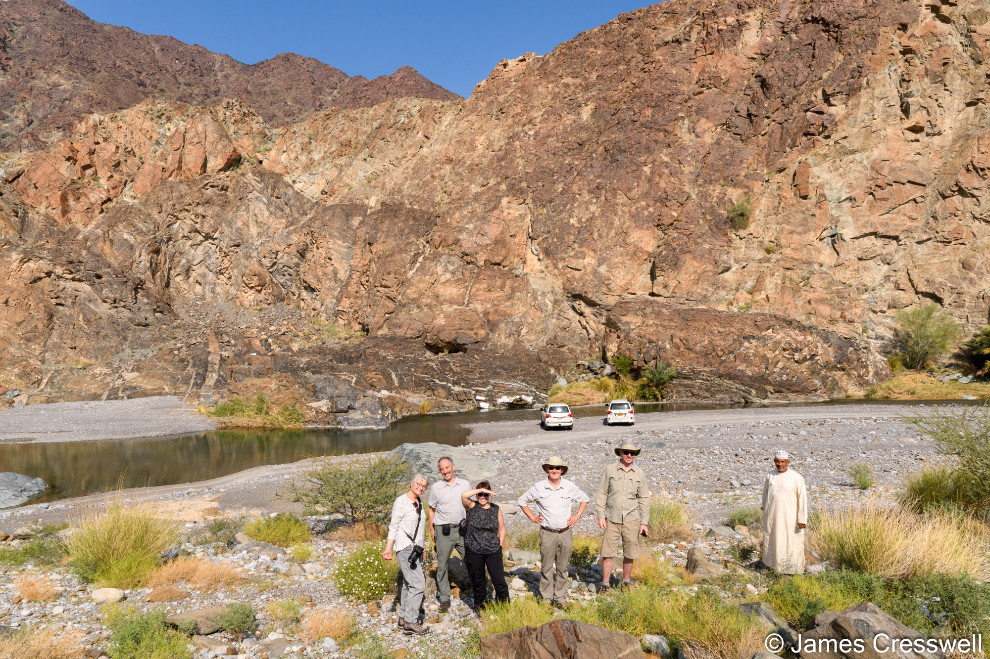 A group of people in front of a stream and a rock outcrop