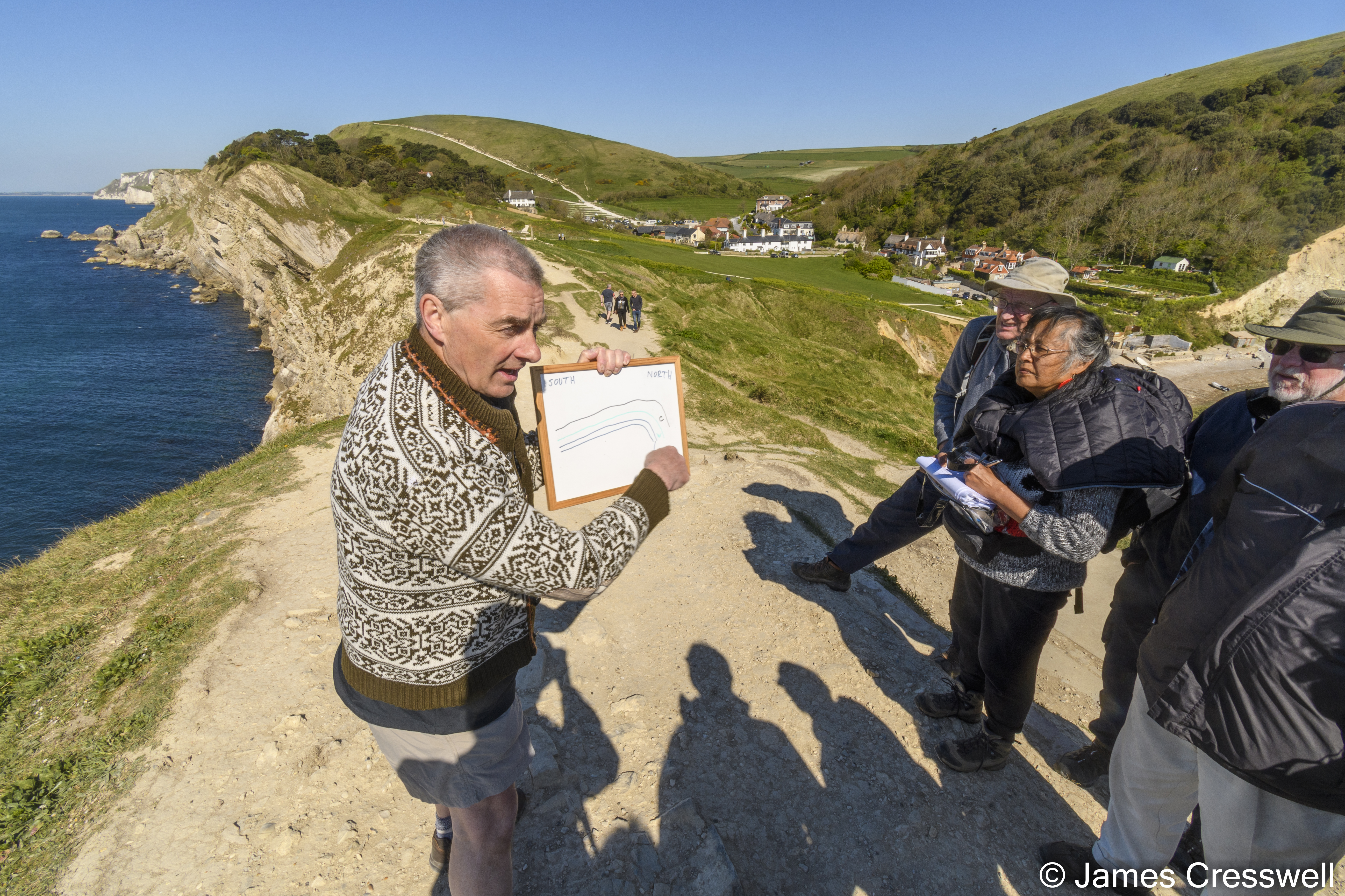 A man explaining geology to a group by the coast