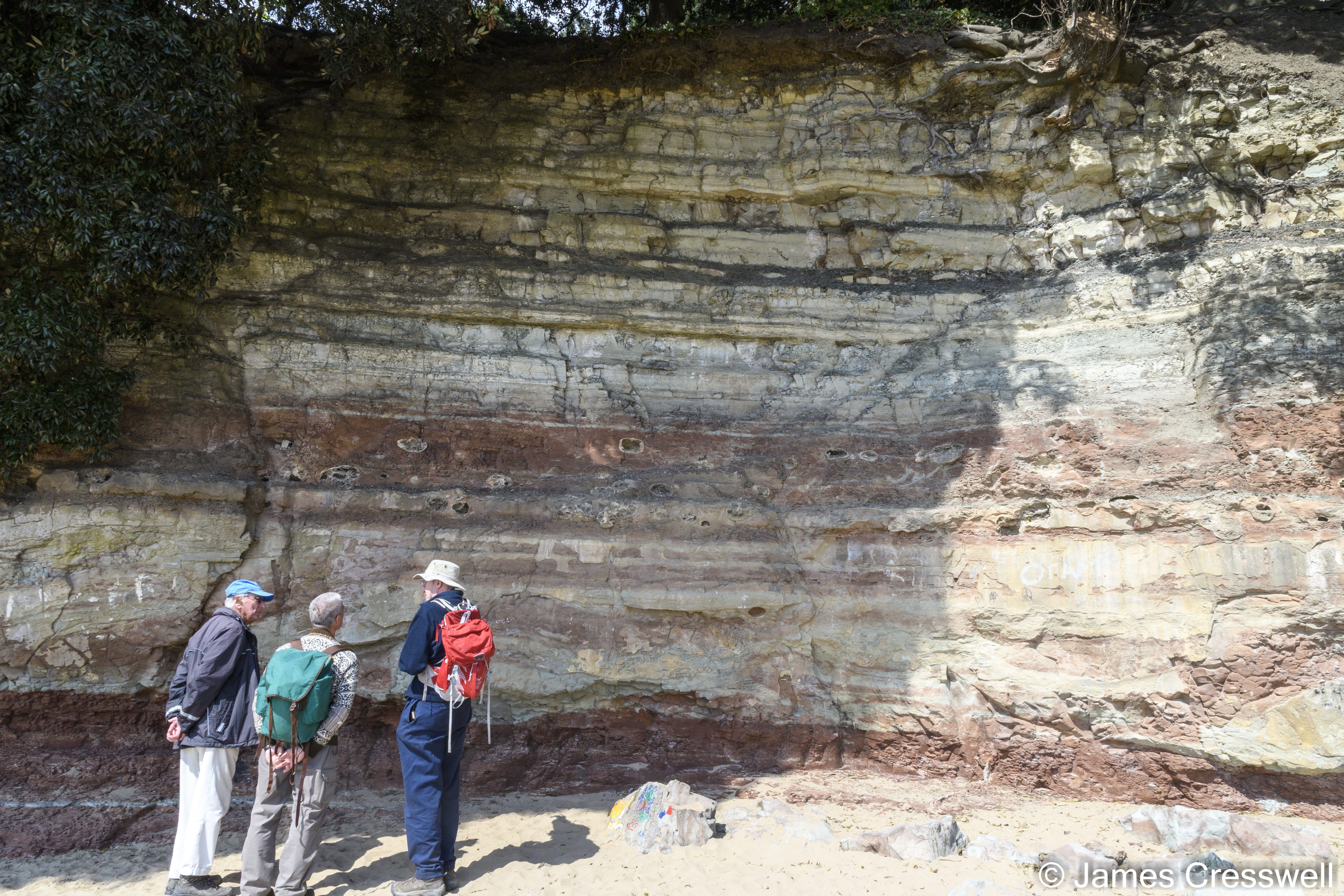 People stand in front of a cliff face with banded rock