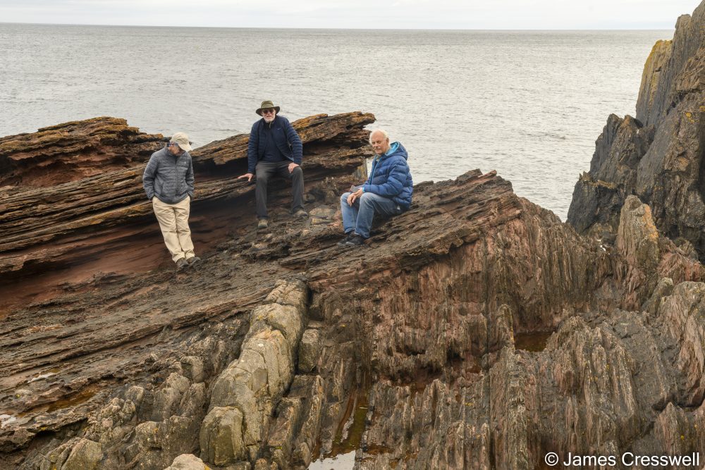 Three men sitting on a rock cliff