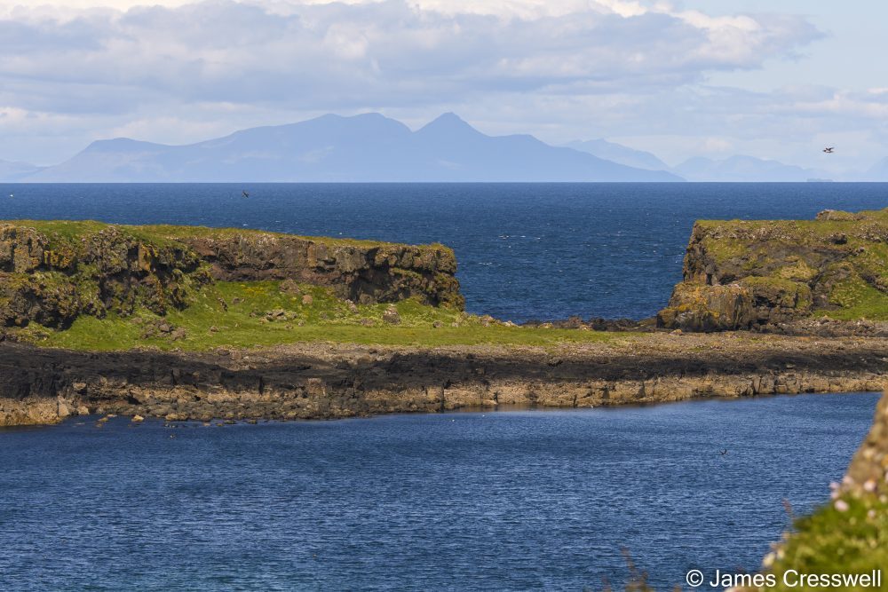 A view across the sea to land, with more sea and mountains in the background