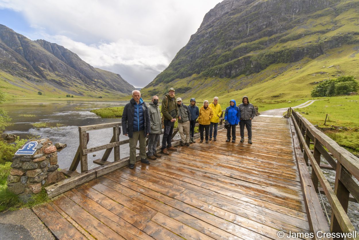Group of people on a bridge acoss a river in a mountainous valley