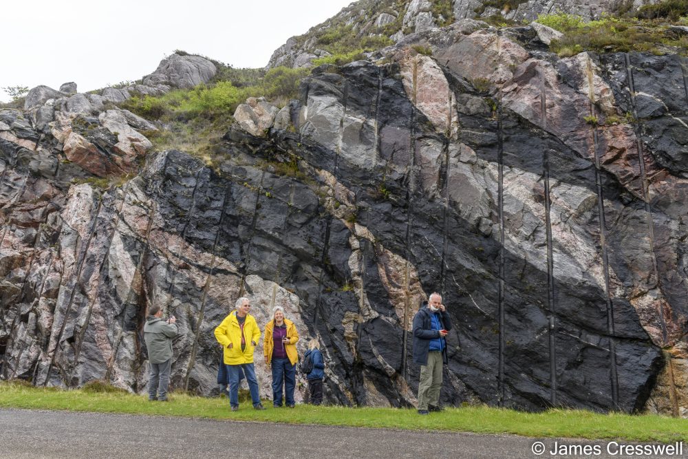 People standing in front of a road cutting in colourful rock