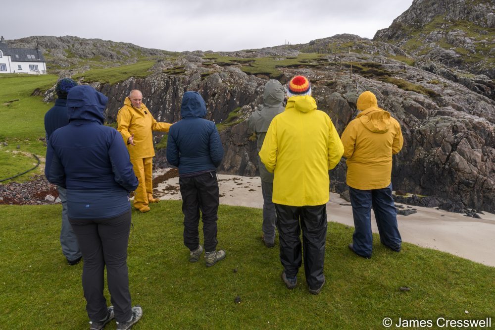Man talking to a group of people by a beach and some rocks