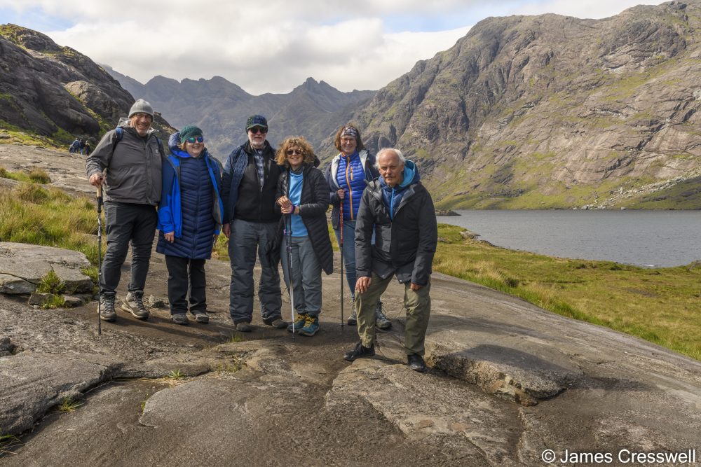 A group of people standing on a rock with a lake and mountain in the background