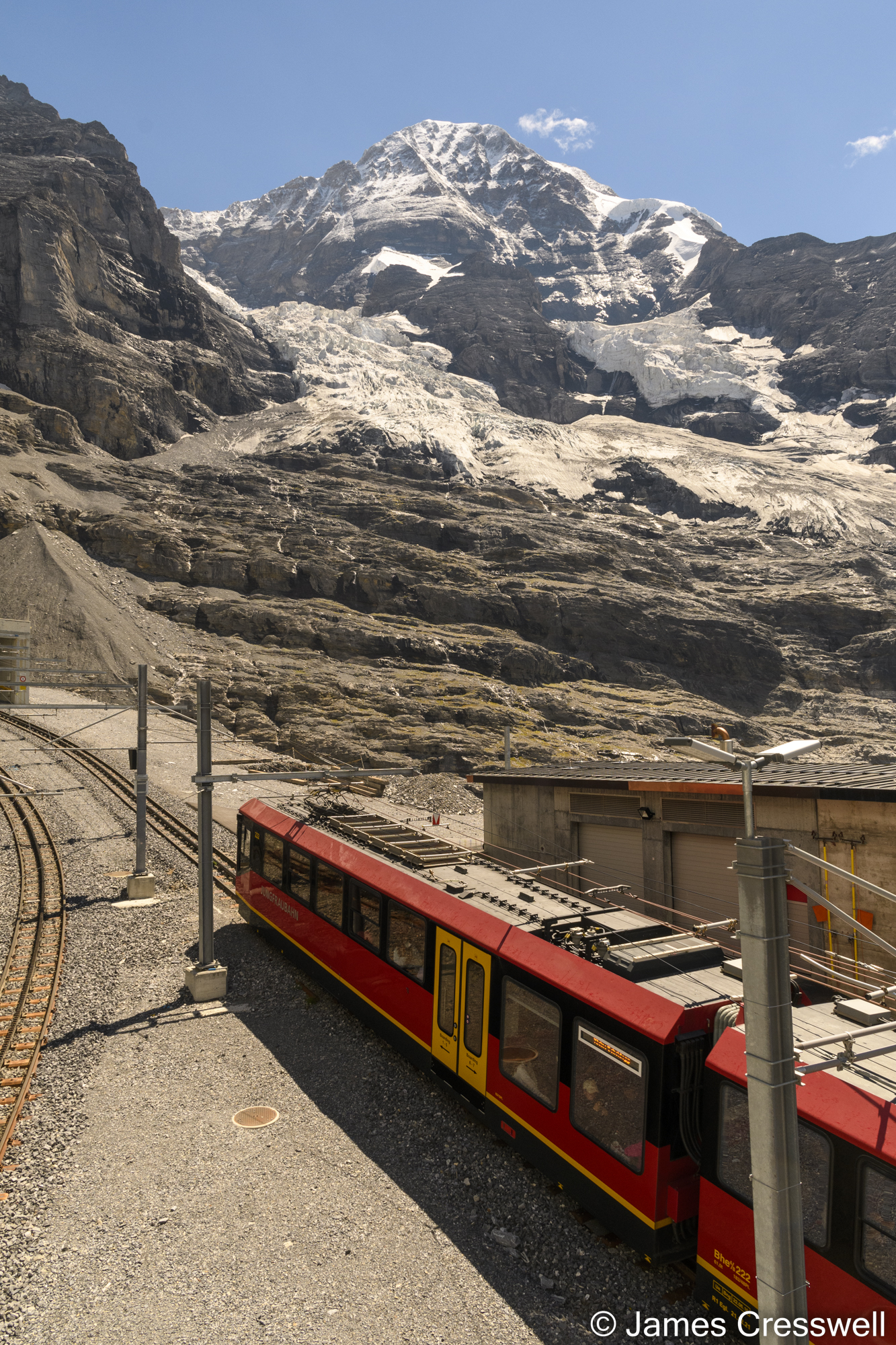 A train at a mountain train station with ice and snow in the background