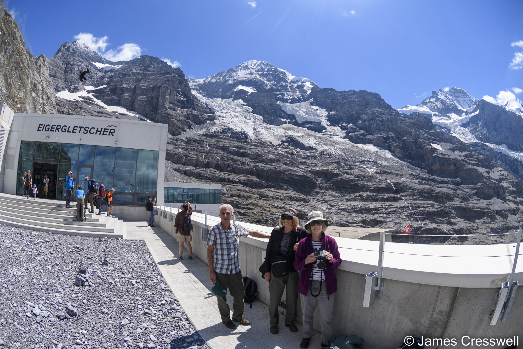 People standing in front of a mountain railway station with mountains in the background