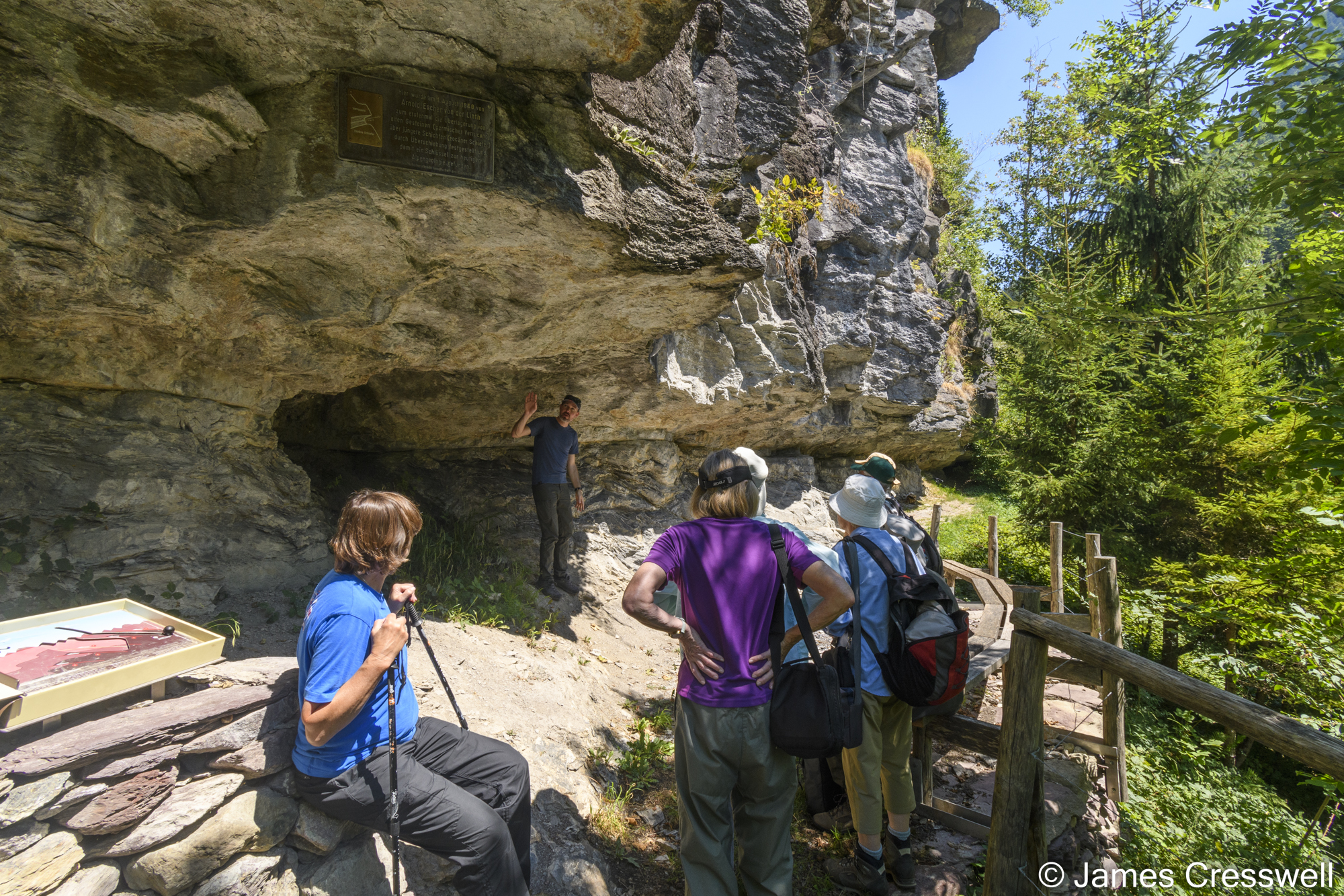 Man standing under a rock overhang explaining to a group