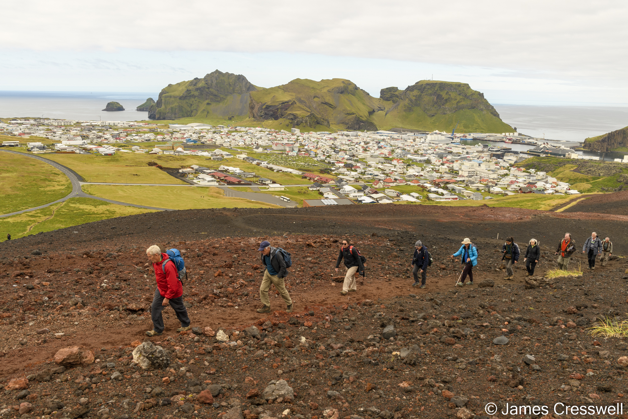 People climbing up a rough track with a town in the background