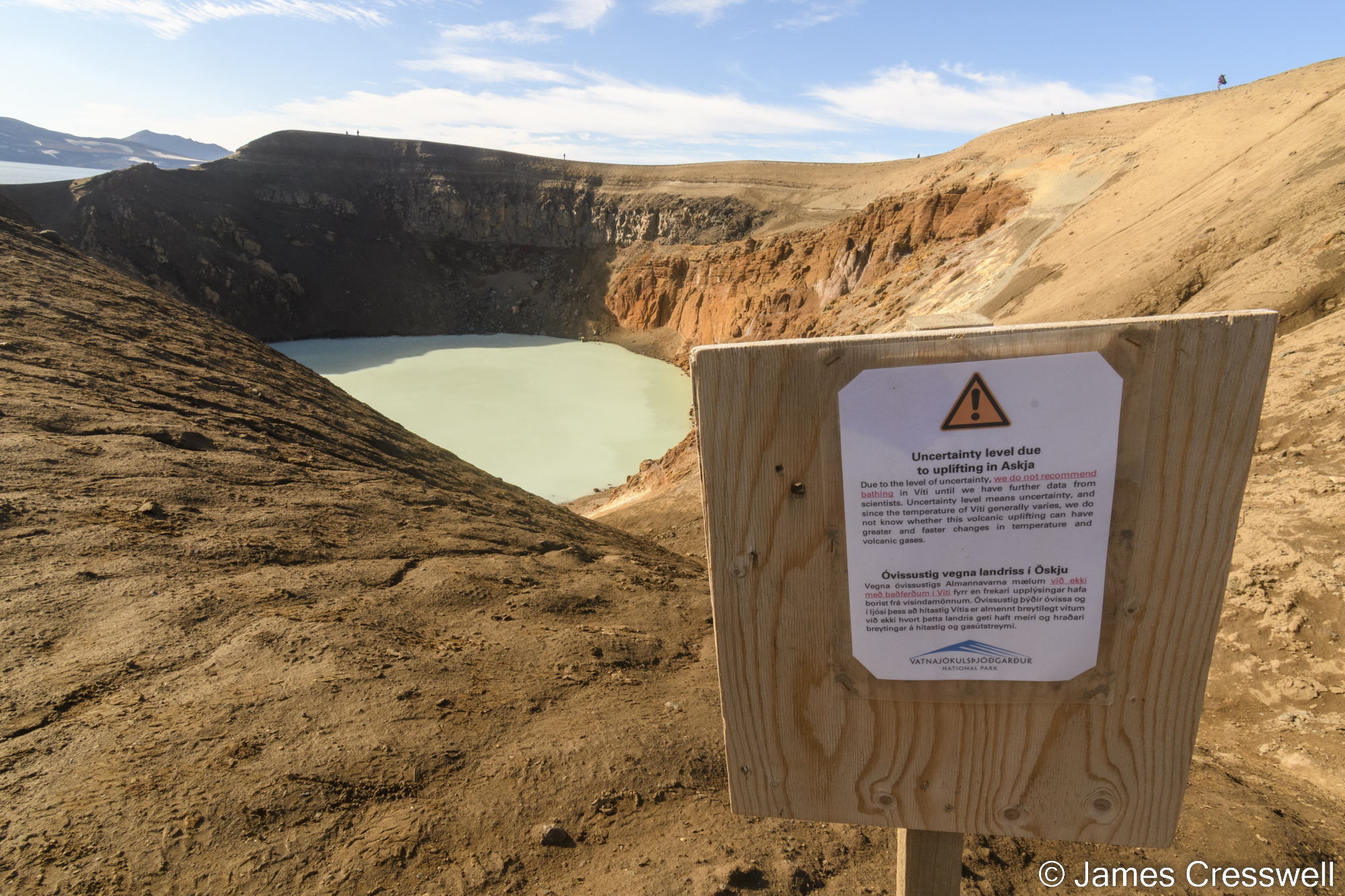 A sign board in front of a water-filled volcanic crater