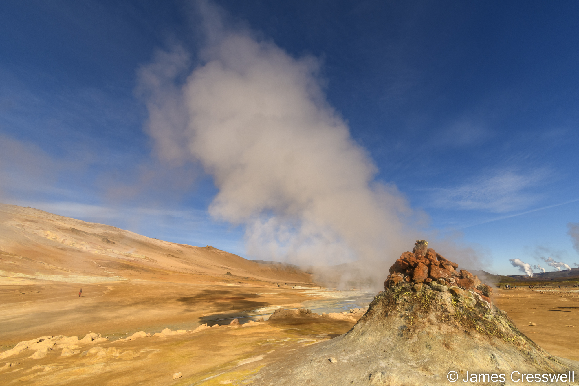 A landscape view with a steaming fumarole in the foreground