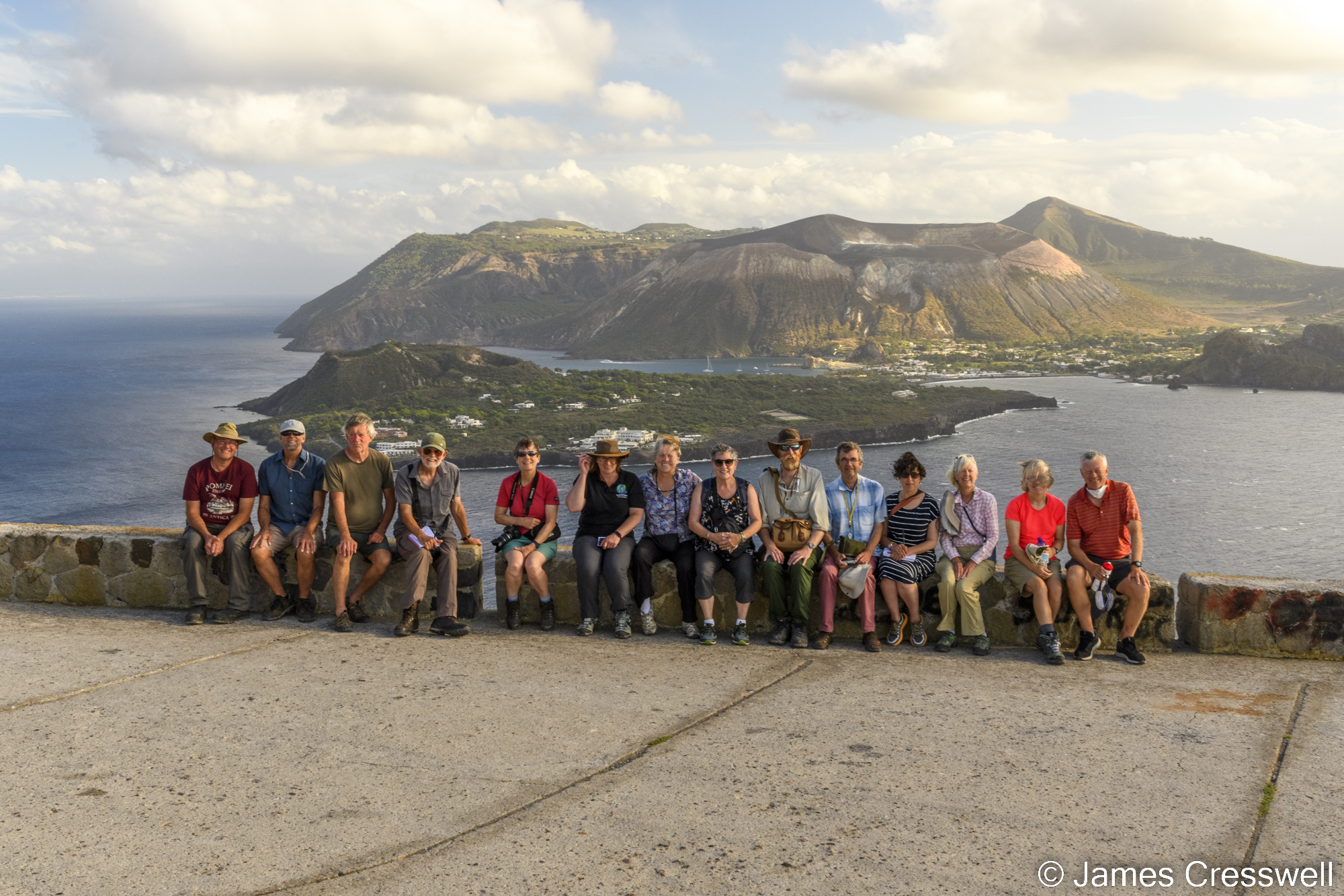 Group of people sitting on a wall with the sea and an island behind them