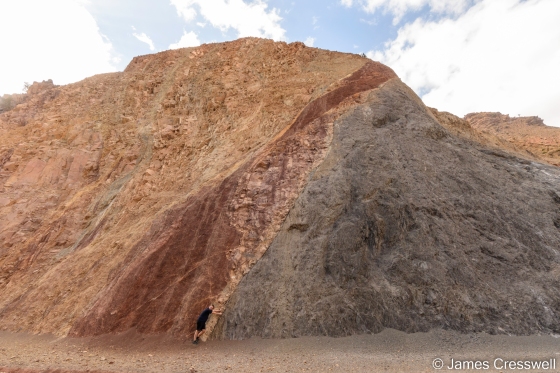 A photo of a fault, with red and yellow rock on the left side and dark grey rock on the right