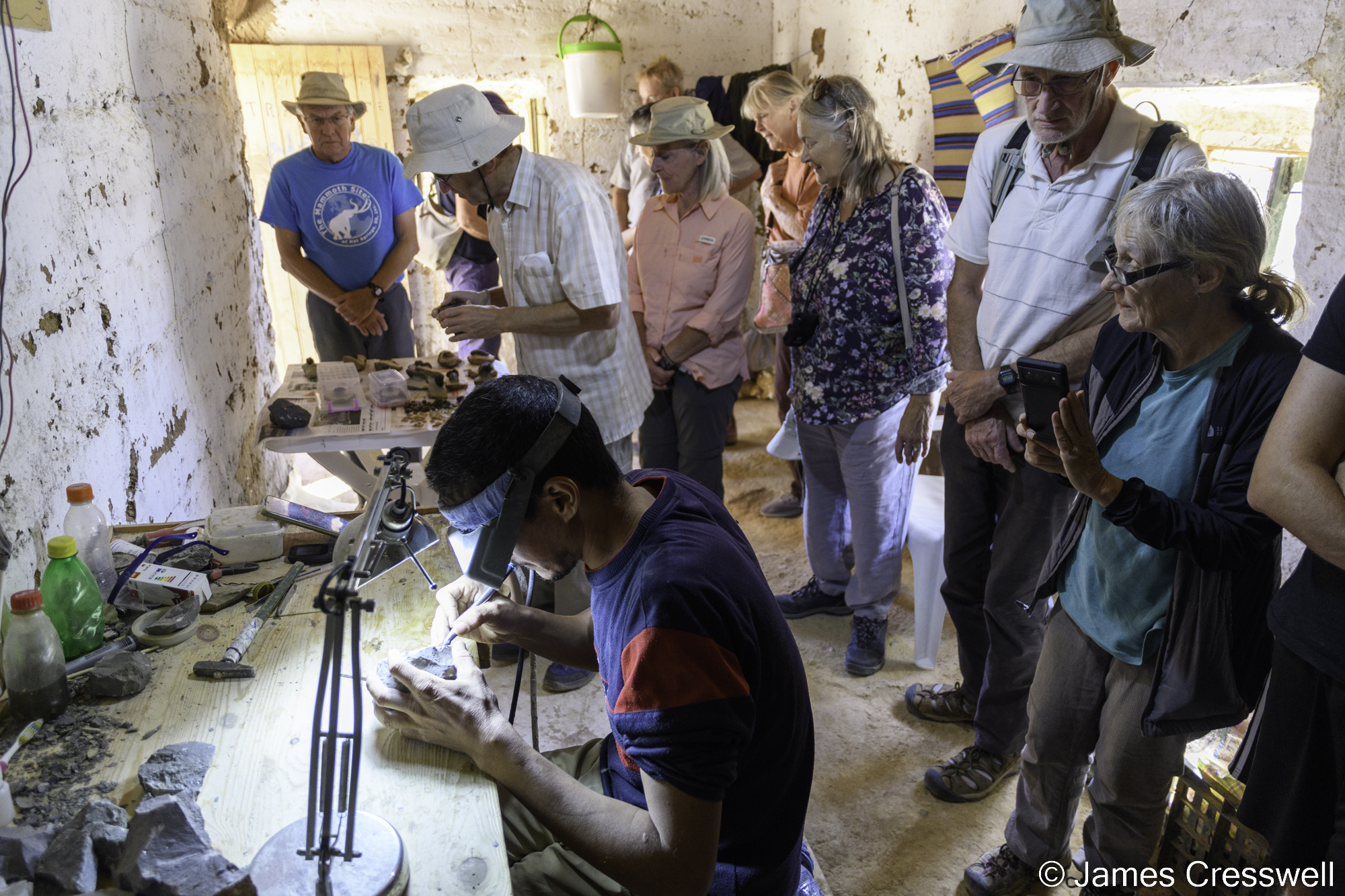 A photograph of tourists observing a man preparing a trilobite