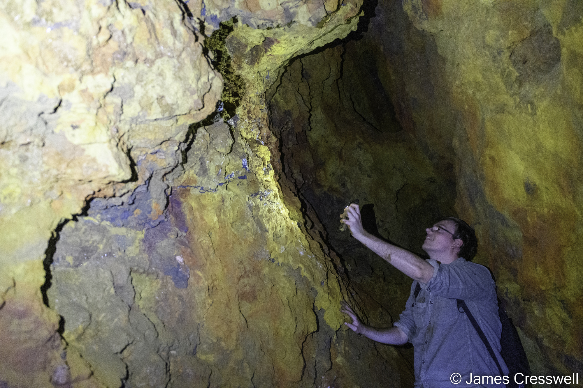 A photograph of a min inside a mine who is illuminating the wall with his mobile phone