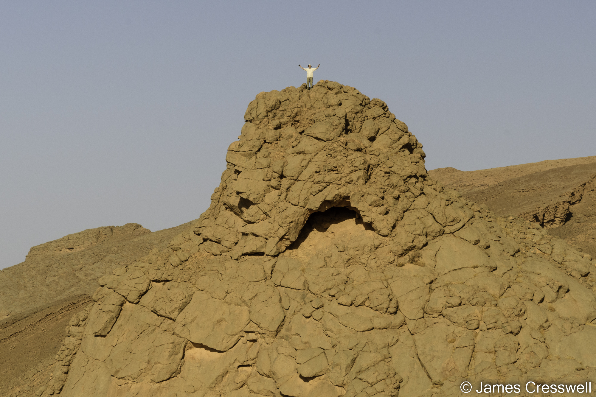 A photograph of a man standing on top of a large rocky outcrop