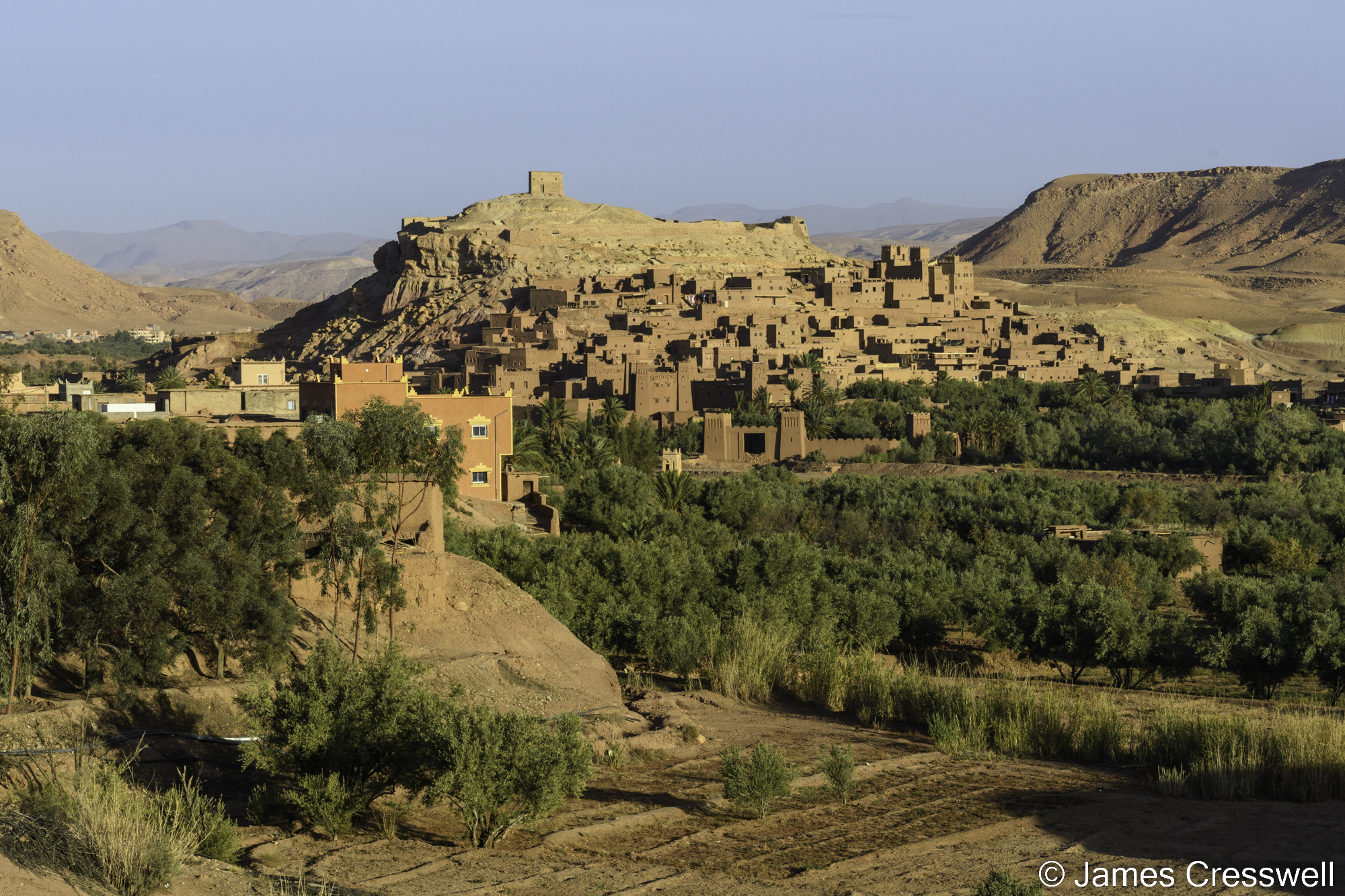 A photograph mud buildings surrounding a hill. There is a tower on the hill top.